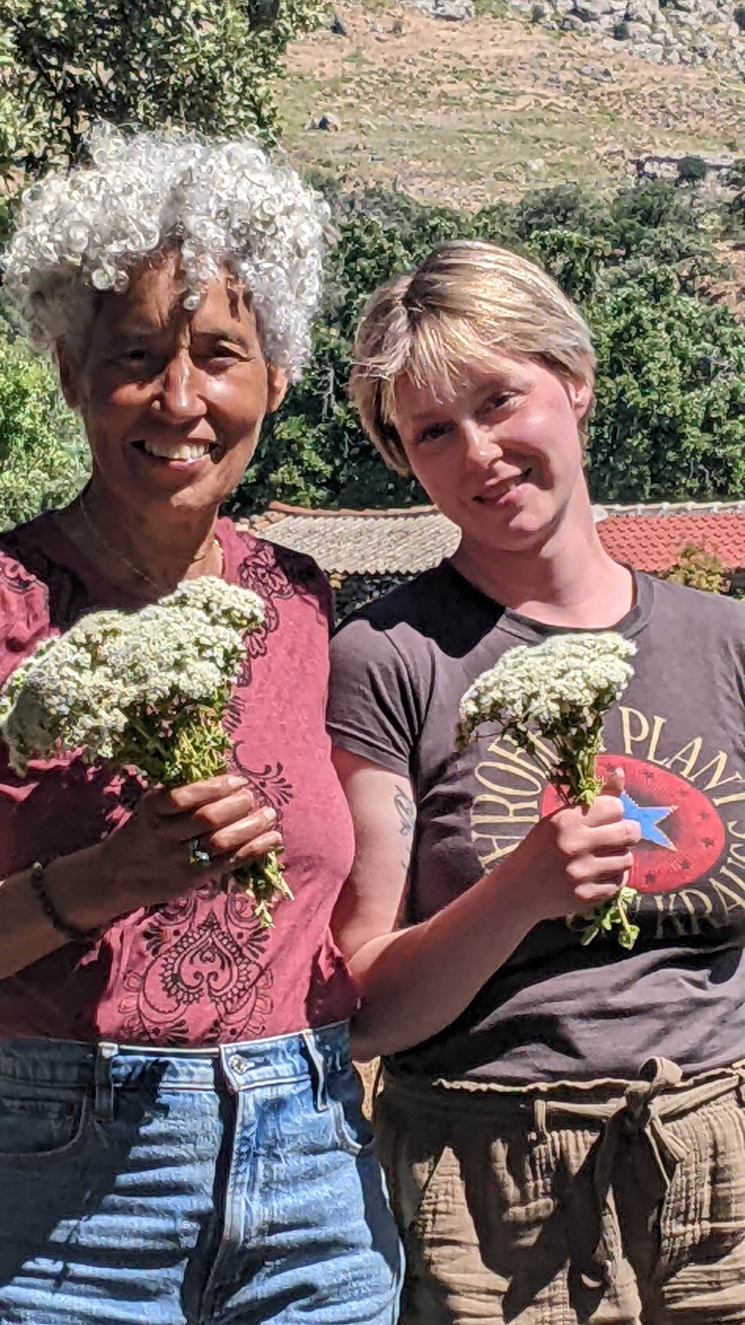 two smiling women holding bunches of white-flowered oregano