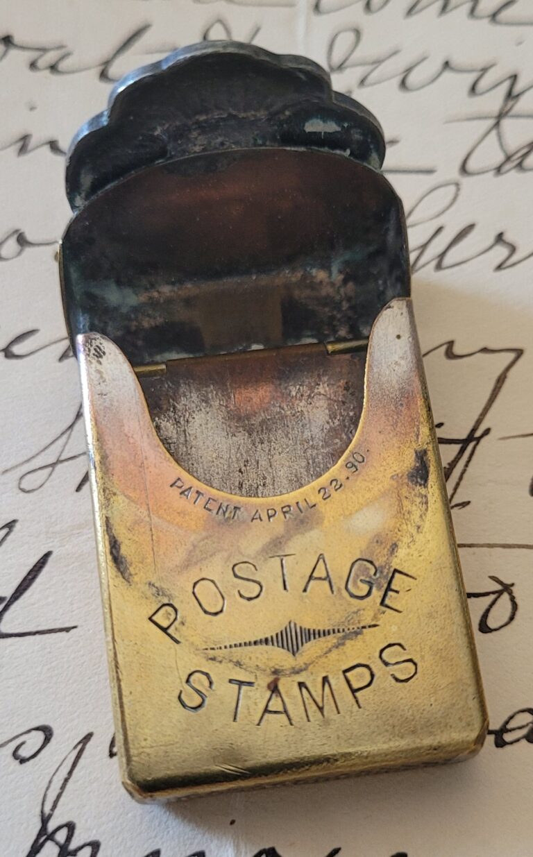 A Victorian silver and brass pocket postage stamp holder lies atop handwritten antique correspondence. 