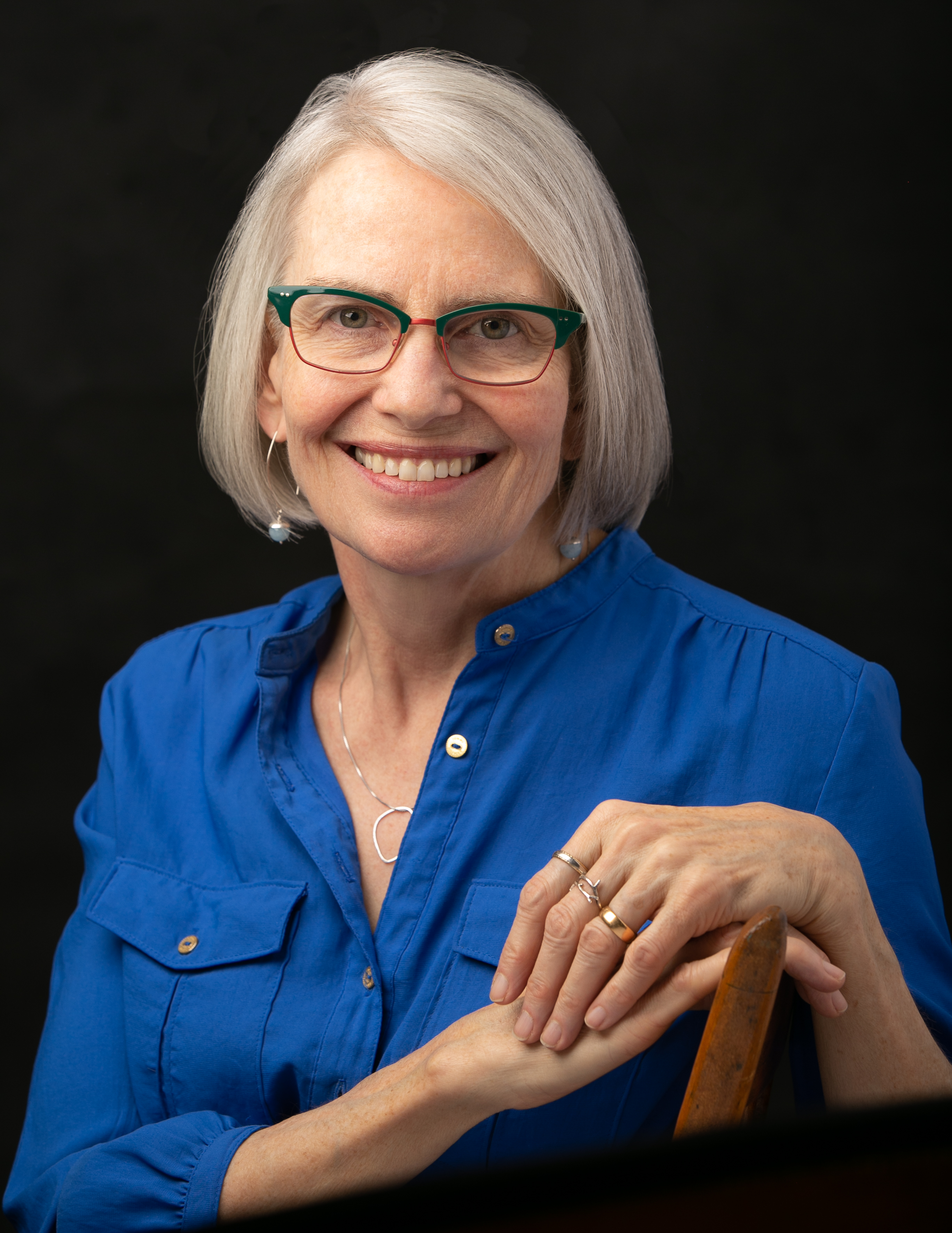 photograph of white woman with white-grey hair, a blue shirt, and green and red glasses